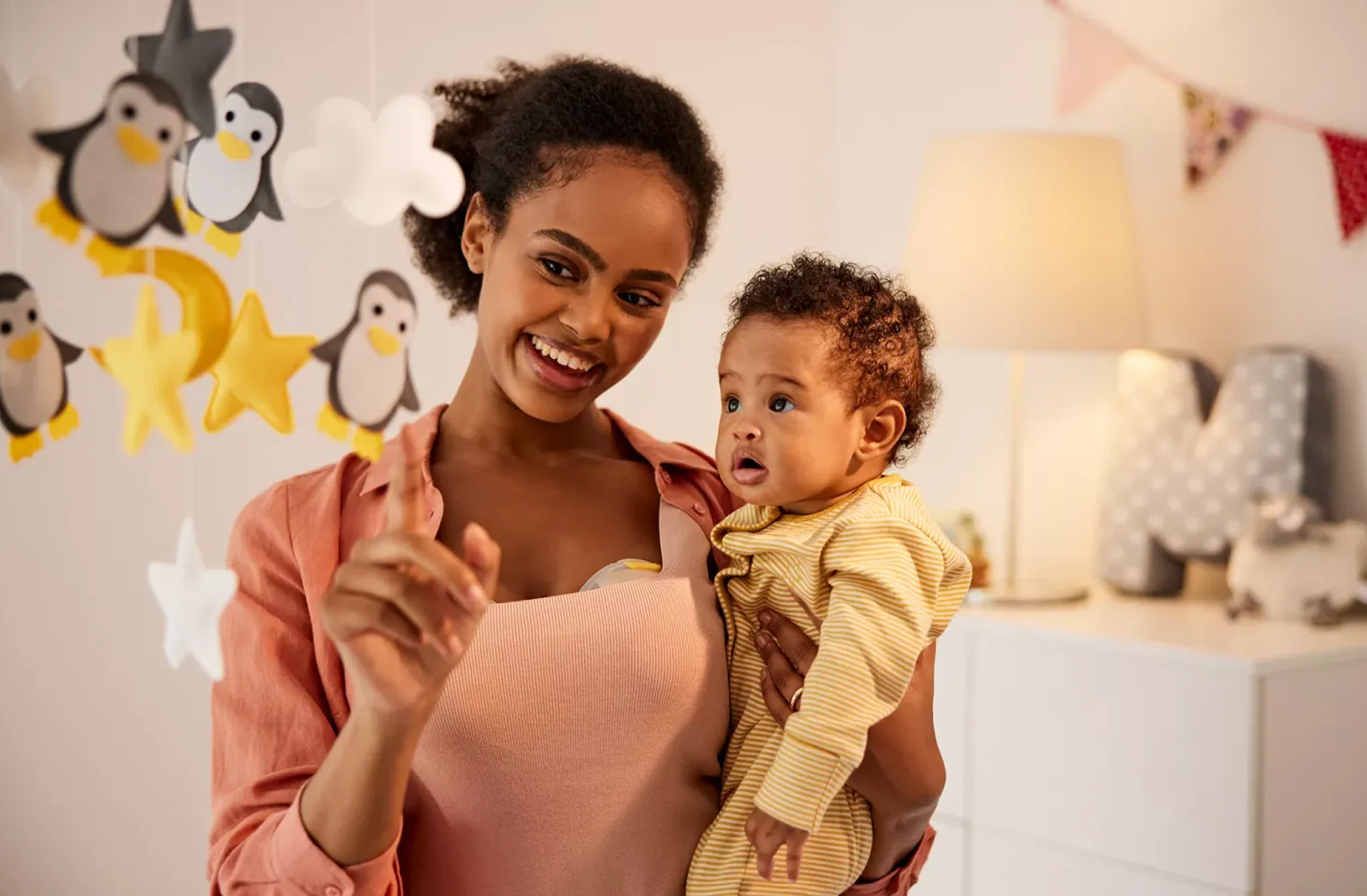woman wearing Portable Breast Pumps holding infant looking at a mobile