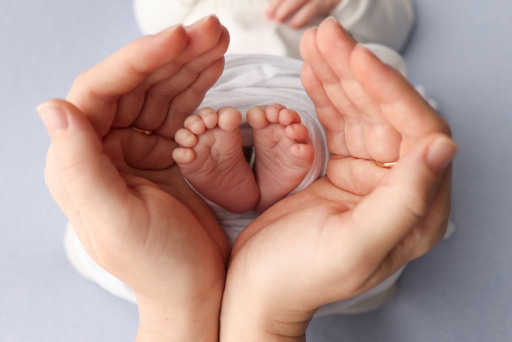 Close-up image of an adult's hands gently cradling a newborn's tiny feet, symbolizing care and nurturing. This image highlights the importance of breast milk benefits for preemies, providing essential nutrients and support for healthy development.