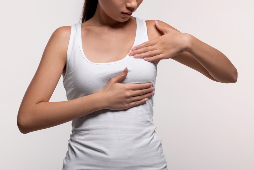 A woman in a white tank top holding her breast, possibly preparing for a breast pump fitting. This image highlights the importance of determining the correct flange size for comfortable and effective breast pumping.